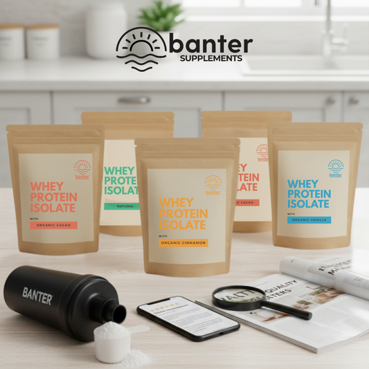 Lineup of Banter Supplements Whey Protein Isolate pouches; Organic Cacao; Organic Cinnamon; Organic Vanilla; Natural; with shaker; scoop and phone on a kitchen bench top; Banter logo above.